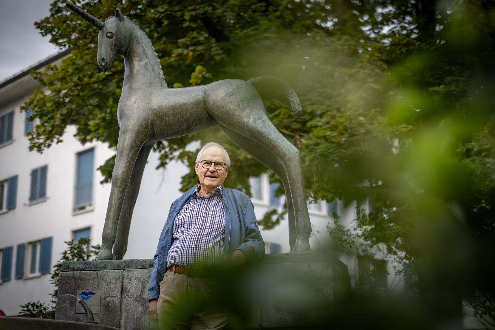 Ein Mann steht vor einer Bronzeskulptur eines Einhorns. 